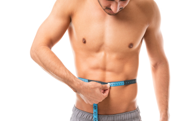 Muscular man measuring his body with tape measure in studio